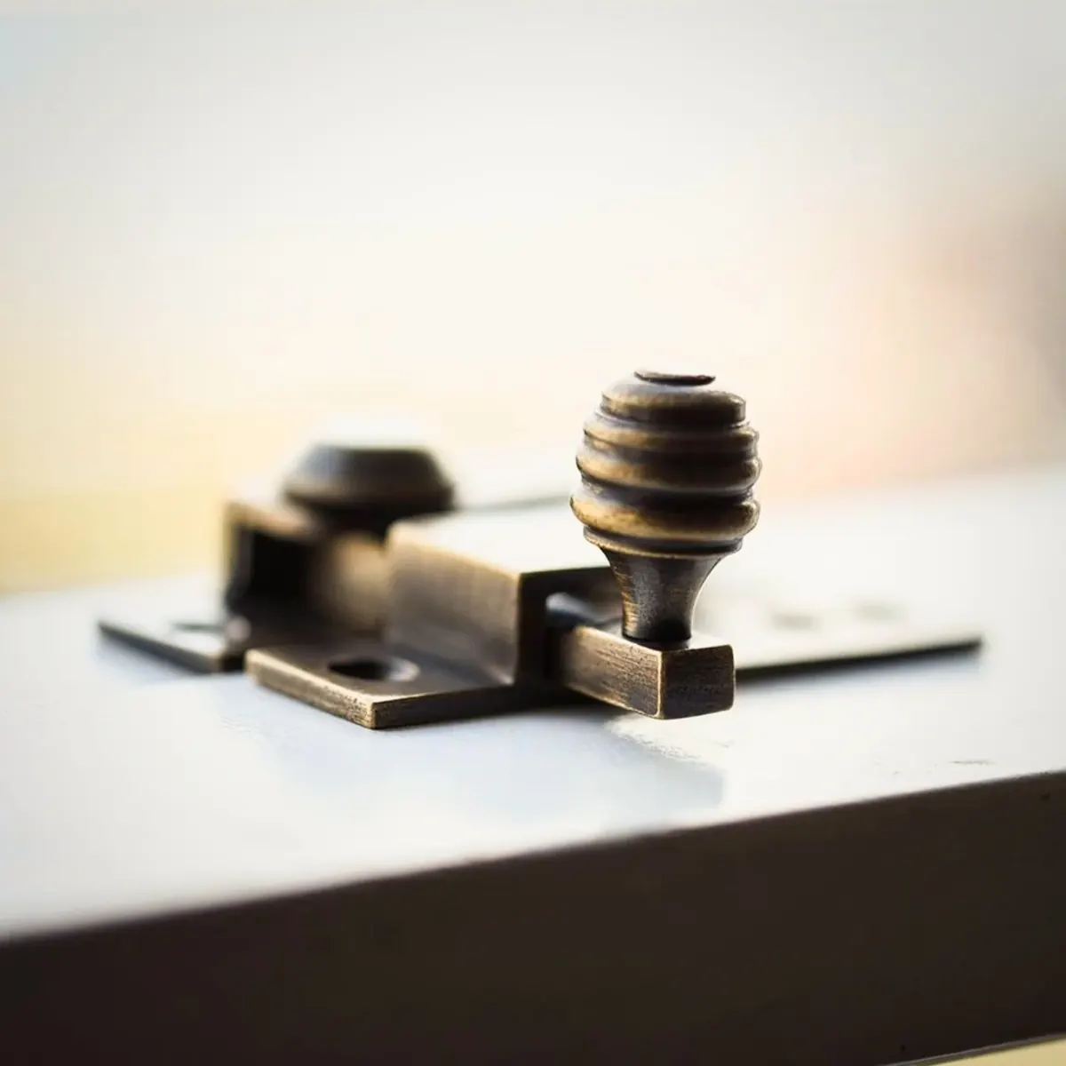 A bronze sash fastener with a beehive knob, closed against the meeting rail