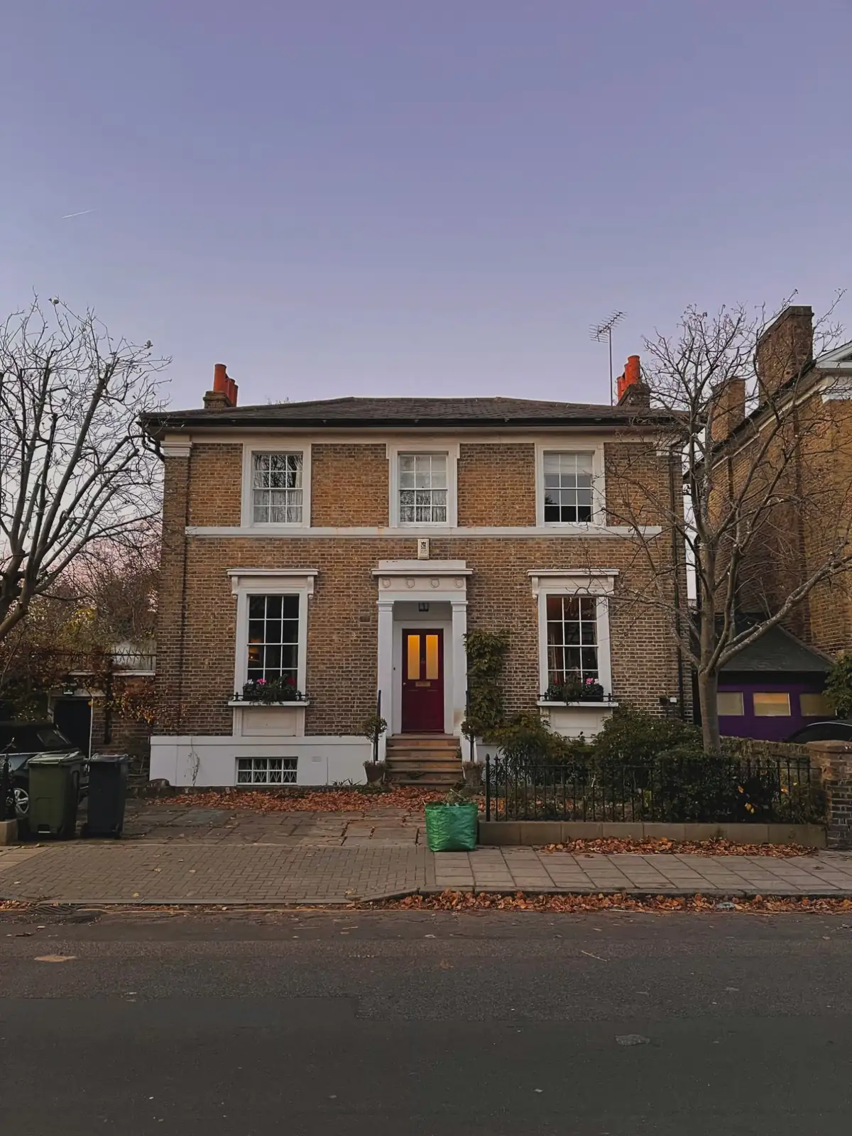 A London brick villa at dusk, its sash windows lit from within above a lamplit doorway