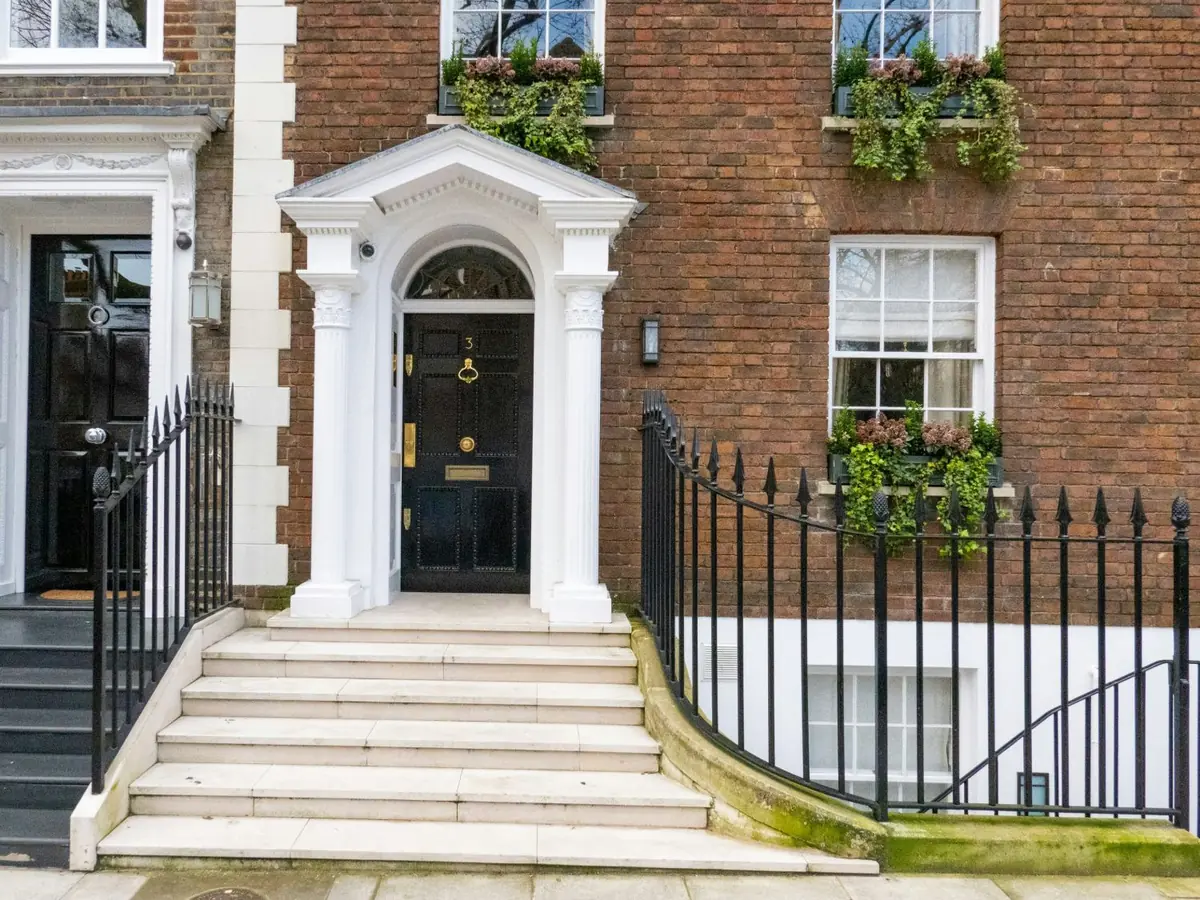 A Georgian doorcase with columns and a fanlight beside a brick elevation of sash windows and window boxes