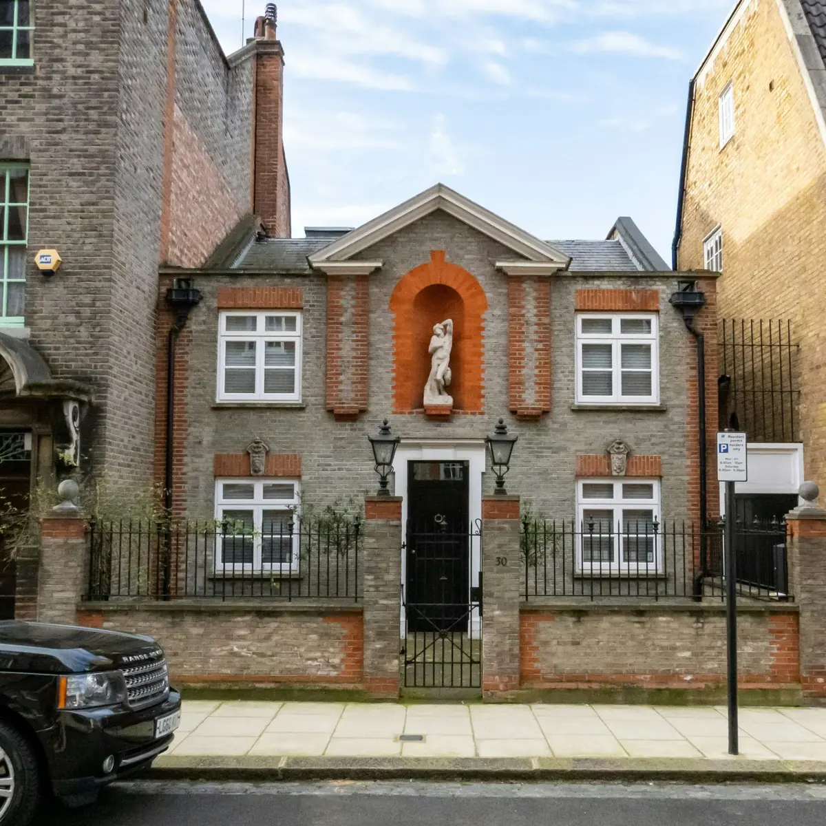 A pedimented brick house with a statue set in an arched niche, white sash windows and iron railings