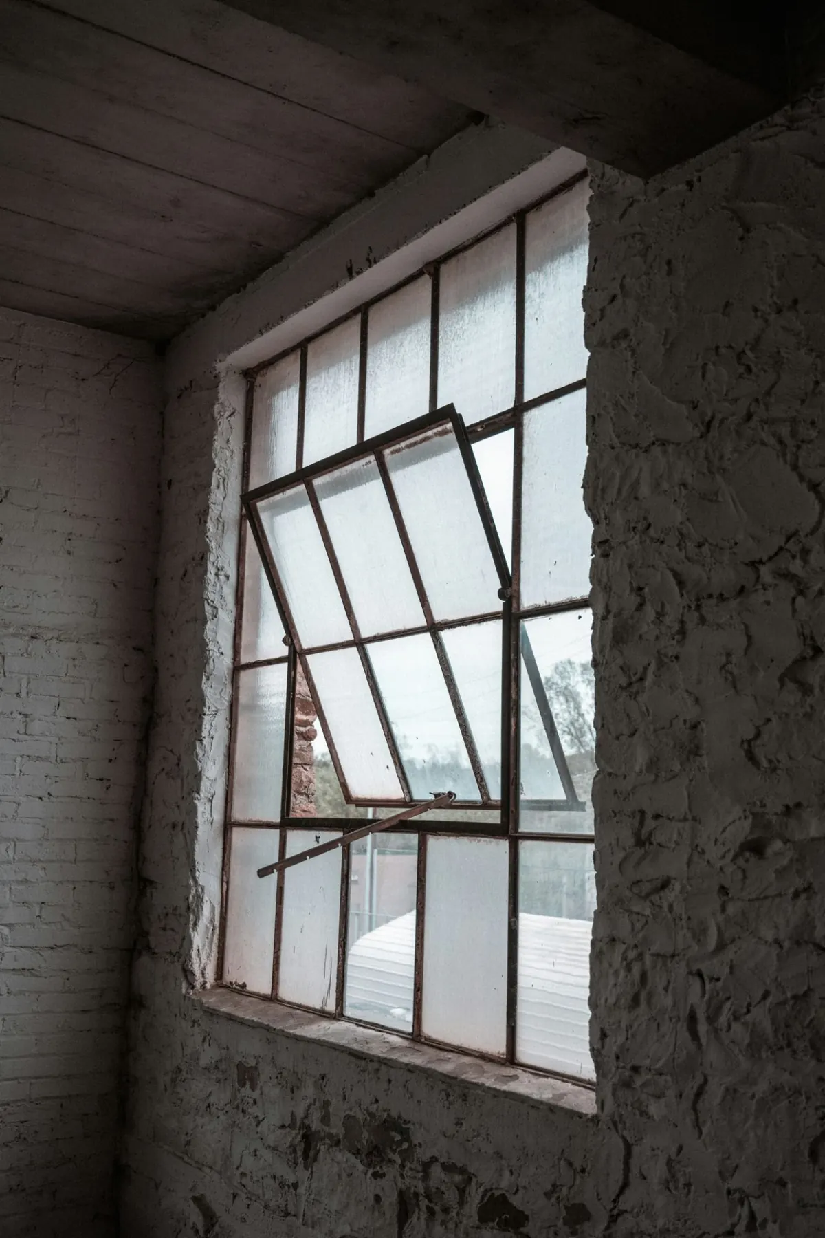 A steel casement with a hopper light propped open on its stay, the frame corroded and the glazing failed