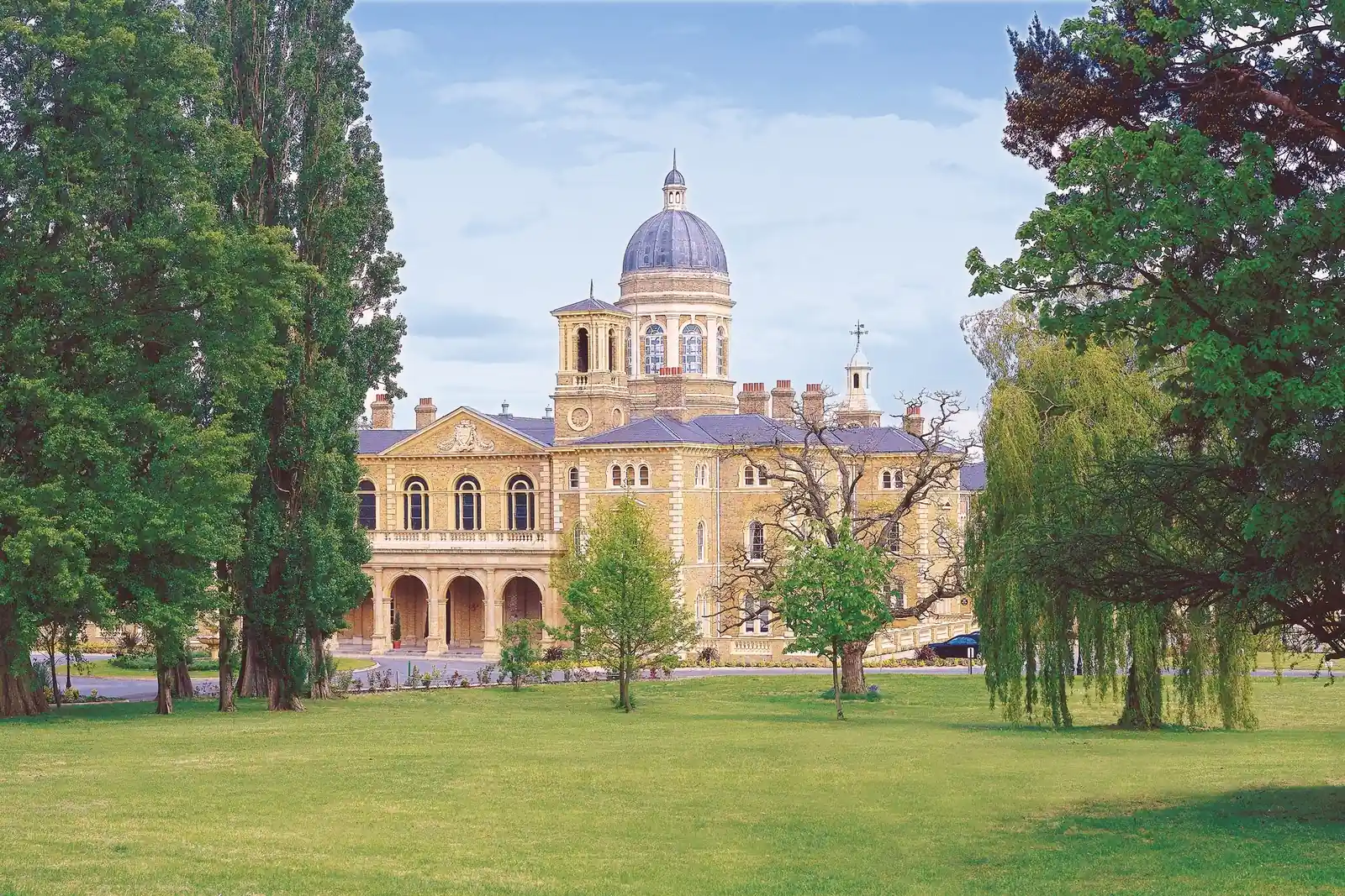 A long nineteenth-century institutional range with a central dome and colonnaded entrance, seen across open parkland