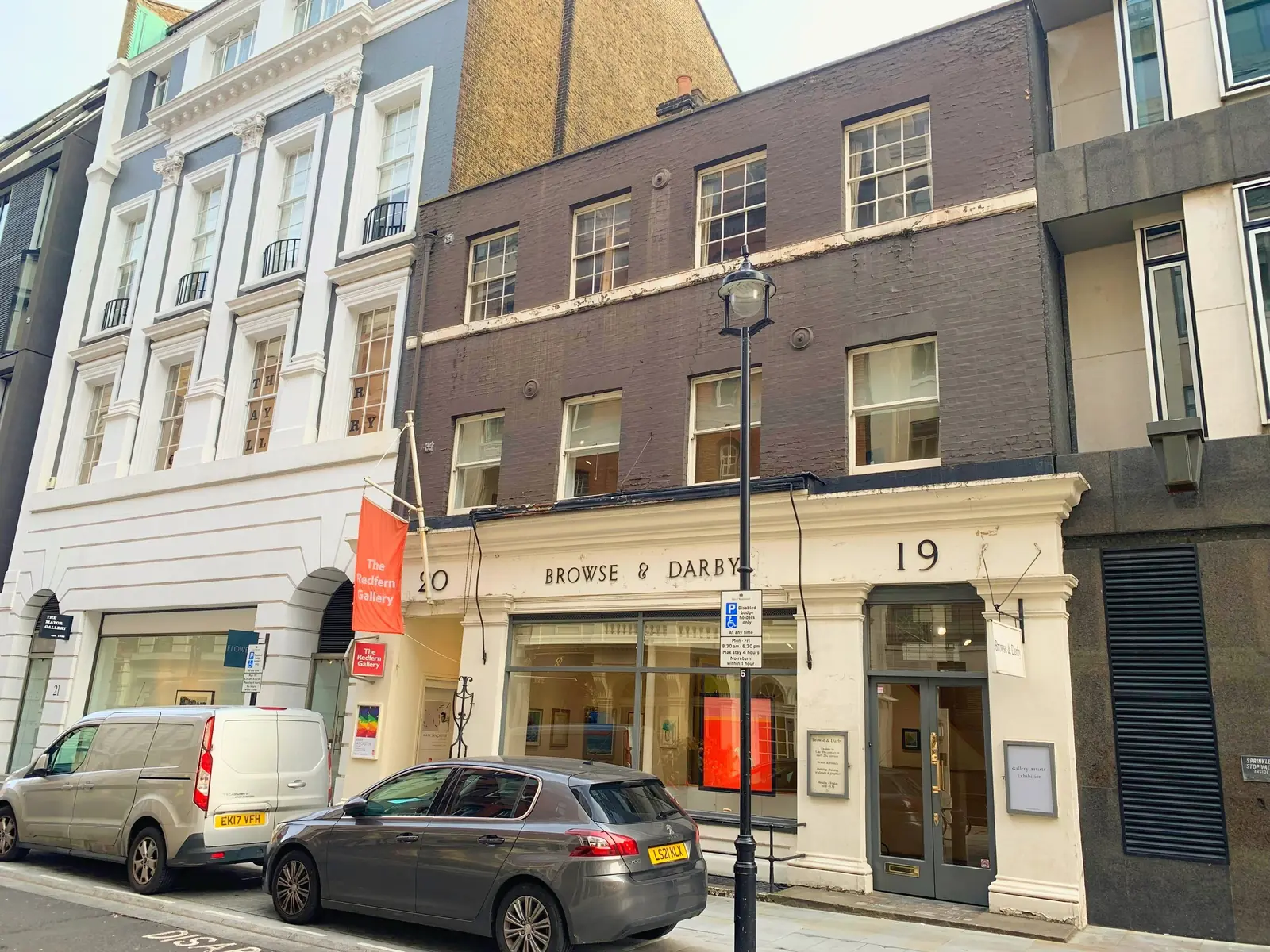 A terrace of gallery frontages, the centre building in painted brick with sash windows over two floors above a stuccoed shopfront