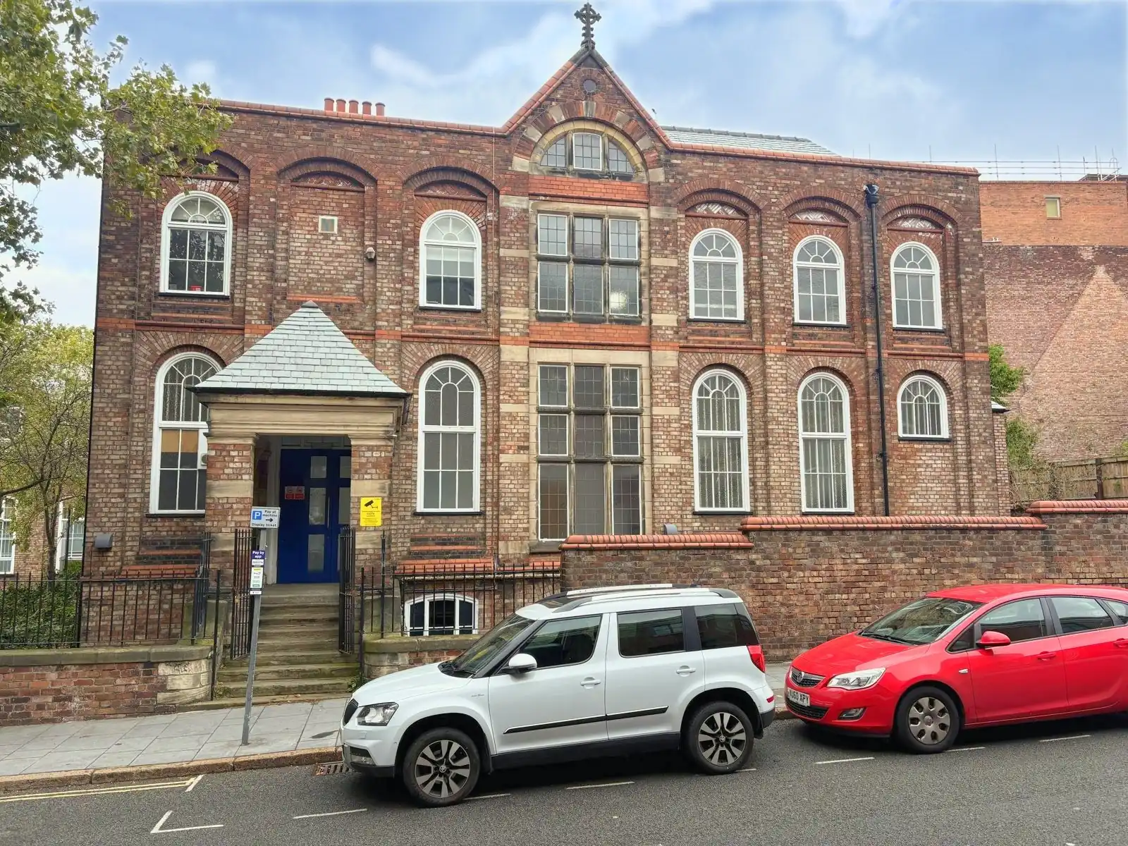 A red brick institutional building with round-arched windows over two floors and a stone-hooded entrance porch